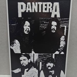 May include: Black and white framed print featuring the band Pantera. The band's name is displayed in large, white, block letters at the top. The image is a collage of four band member portraits. The frame is white.