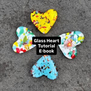 以下が含まれることがあります： モザイクデザインのカラフルなガラス製のハートペンダントが4つ、灰色の表面に配置されています。 ハートは黄色、青、白で、花柄や抽象的な模様があります。 画像のテキストは「Glass Heart Tutorial E-book」です。
