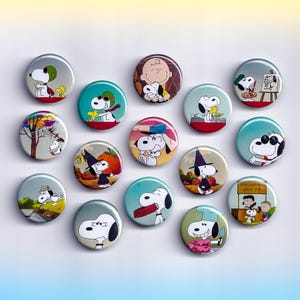 May include: A collection of round Snoopy character buttons. Each button features a different Snoopy design, including Snoopy with Woodstock, Snoopy in various outfits, and Snoopy with Charlie Brown. The buttons are in various colors and sizes.