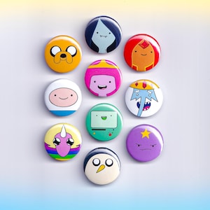 May include: A collection of Adventure Time character button pins. The pins feature characters like Jake, Finn, Princess Bubblegum, and Ice King. Each pin is a different color and design, with a glossy finish.