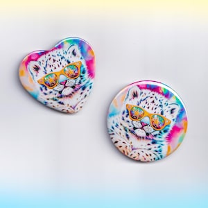 May include: Two colorful buttons featuring a white leopard wearing star-shaped sunglasses. One button is heart-shaped, the other is round. The buttons have a tie-dye background with pink, blue, and yellow hues.
