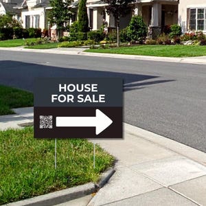 May include: A black and grey "HOUSE FOR SALE" sign with a white arrow and QR code is placed in front of a green lawn. The sign is on metal stakes. Houses and a street are in the background.