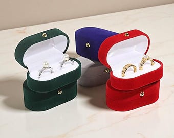 Puede incluir: Varias cajas de anillos de terciopelo en verde, rojo, azul y gris están abiertas, mostrando anillos. Las cajas tienen un cierre dorado y un interior blanco. Los anillos incluyen un anillo de perlas y anillos de oro con piedras preciosas.
