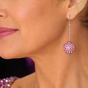 May include: A dangling earring featuring a spherical charm covered in small, light pink crystals. The sphere is suspended from a silver-toned metal chain and a hook-style finding, creating a drop-style design that hangs vertically from the earlobe.