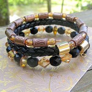 May include: Three layered bracelets with black leather, gold and copper toned beads, and clear and black glass beads.