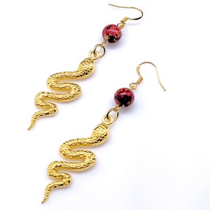 May include: Gold snake dangle earrings with red and gold speckled beads.