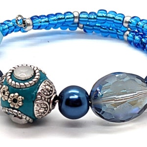 May include: A blue and turquoise beaded bracelet with silver accents. The bracelet features a variety of beads, including round, faceted, and decorative beads.