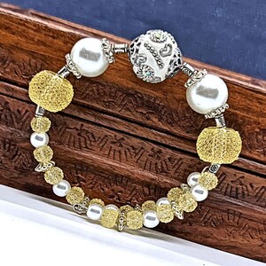 May include: A bracelet with white and yellow beads. The bracelet has a silver charm with a heart design and the word "love" written on it.