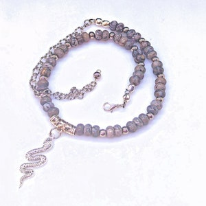 May include: A silver snake charm hangs from a layered necklace with brown and silver beads.