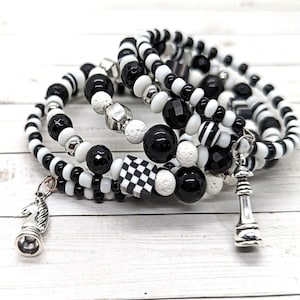 May include: A set of five black and white beaded bracelets with a chess piece charm. The bracelets are made with different types of beads, including black and white glass beads, white lava beads, and black onyx beads.