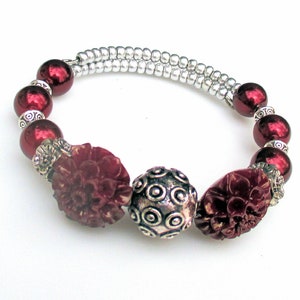 May include: A red and silver beaded bracelet with two large red flower-shaped beads and a silver bead with a circular pattern.