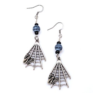 May include: Silver spider web earrings with a blue and black bead. The spider web is detailed with a small silver spider.