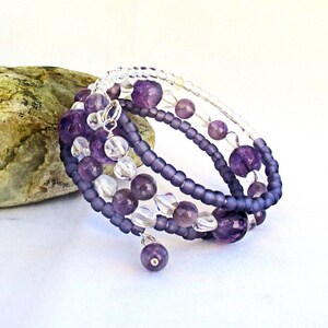 May include: A multi-strand bracelet with amethyst and clear beads. The bracelet is wrapped around a gray rock.