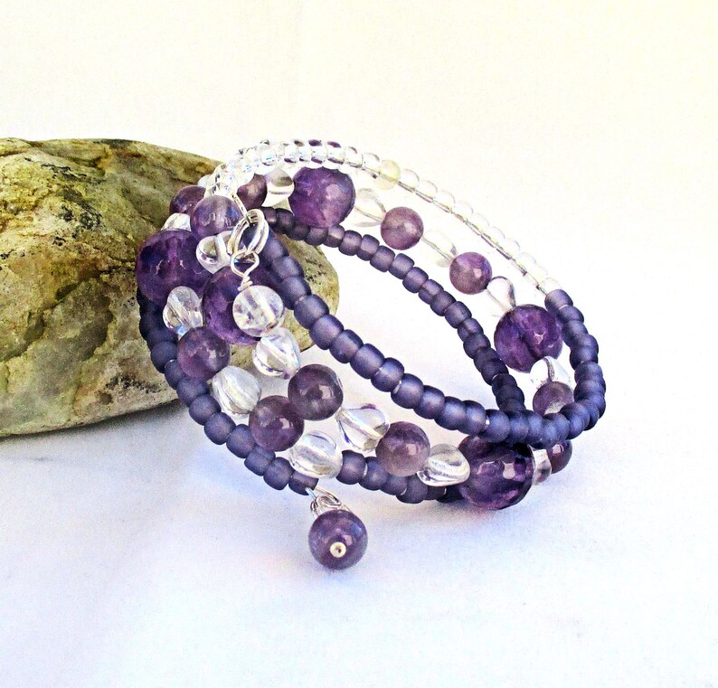 May include: A multi-strand bracelet with amethyst and clear beads. The bracelet is wrapped around a gray rock.
