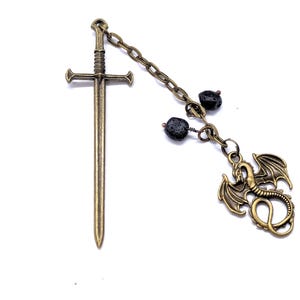 May include: A bronze-colored bookmark featuring a sword design with a chain, two black beads, and a dragon charm. The bookmark is set against a white background.