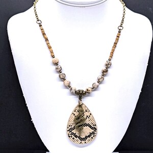 May include: A brown and white beaded necklace with a snake-shaped pendant. The pendant is made of leather and has a brown and white pattern.