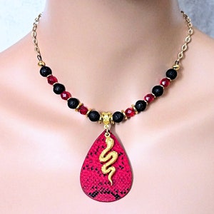 May include: A red and black necklace with a gold snake pendant. The necklace is made with lava rock beads and red glass beads. The pendant is a teardrop shape with a gold snake design.