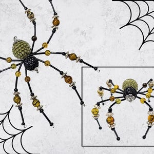 May include: A decorative spider ornament featuring a green crystal-encrusted abdomen and a black crystal-encrusted thorax. The eight legs are constructed from black wire accented with amber-colored beads and silver-toned metal spacers.