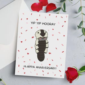 以下が含まれることがあります： 「YIP YIP HOORAY」と「H-APPA ANNIVERSARY！」の文字が入った白いグリーティングカード。生き物の漫画イラストが特徴です。カードは赤いハートと紙吹雪で飾られています。赤いバラと緑の植物が背景にあります。