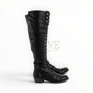 May include: A pair of black leather knee-high boots with lace-up detailing and a low heel. The boots have a classic design with a rounded toe and are suitable for various occasions. The word "VE" and the word "LEATHER" are visible on the side of the boots.