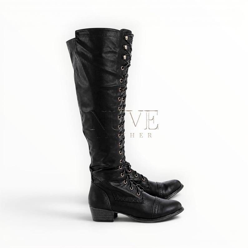 May include: A pair of black leather knee-high boots with lace-up detailing and a low heel. The boots have a classic design with a rounded toe and are suitable for various occasions. The word "VE" and the word "LEATHER" are visible on the side of the boots.