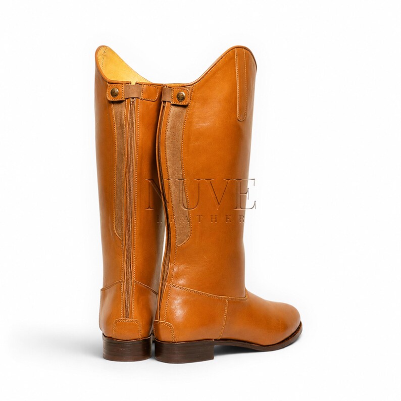 May include: A pair of tall, tan leather riding boots. The boots have a classic design with a high shaft, a rounded toe, and a small heel. The boots feature a zipper on the back and are made of smooth, polished leather.