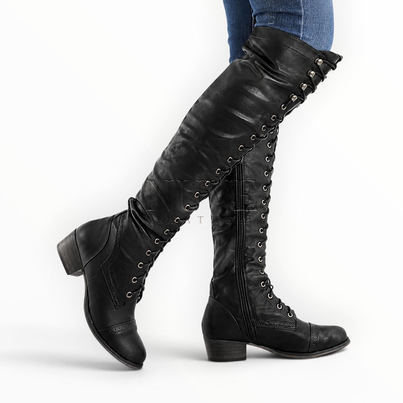 May include: Black knee-high boots with a lace-up design and a small heel. The boots have a zipper on the side and are made of a smooth material. The boots are worn with blue jeans.