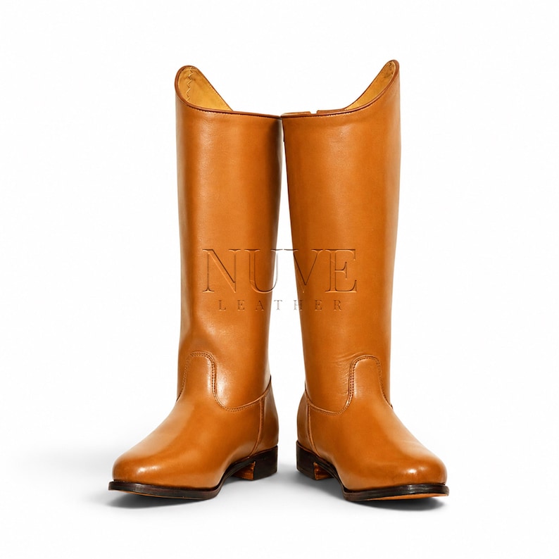 May include: A pair of tall, tan leather riding boots. The boots have a smooth finish, a rounded toe, and a small heel. The shaft of the boots is tall, reaching up to the mid-calf. The boots have the text "NUVE LEATHER" embossed on the side.