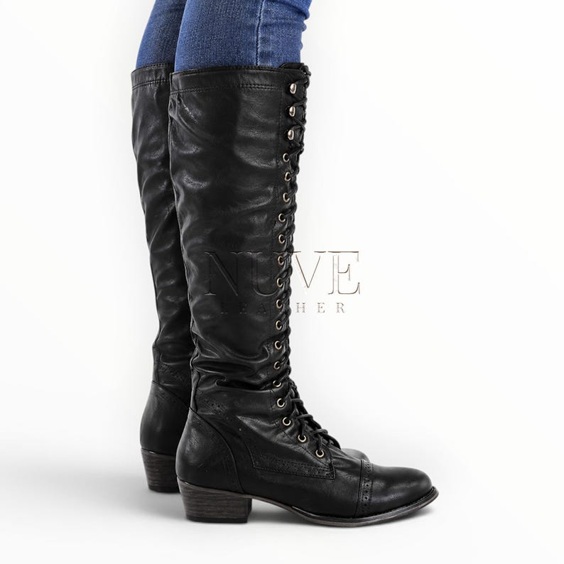 May include: Black leather knee-high boots with lace-up detailing and a small heel. The boots have a classic design with a rounded toe and a textured finish. The boots are worn with blue jeans.