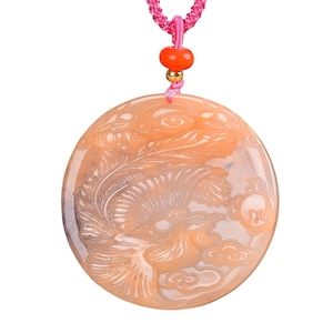 May include: A round, peach-colored pendant necklace with a carved phoenix design. The pendant is suspended from a pink braided cord with an orange bead and gold-colored accents. The phoenix is detailed with feathery wings and cloud motifs.