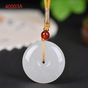 May include: A white jade pendant with a circular design and a central hole. The pendant is suspended from a gold-coloured cord, accented with a red bead and a gold-coloured clasp. The text "40003A" is visible in the upper left corner.