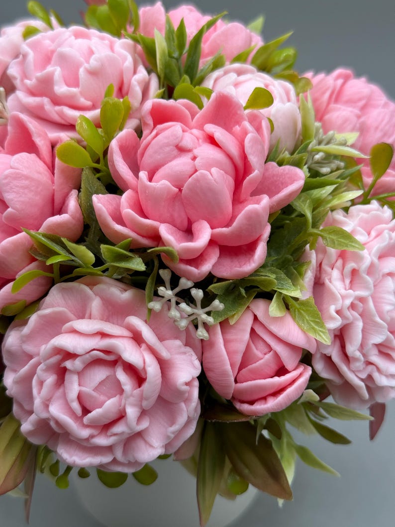 Pode incluir: Um close-up de um buqu&ecirc; de flores de pe&ocirc;nia rosa com folhas verdes. As flores est&atilde;o em plena flora&ccedil;&atilde;o, com p&eacute;talas delicadas e uma cor pastel suave. O arranjo &eacute; exuberante e cheio, com uma variedade de texturas e tons de rosa.