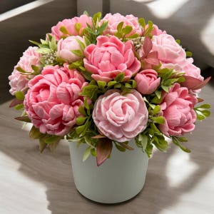 Pode incluir: Um buqu&ecirc; de flores de pe&ocirc;nia rosa em um vaso de cer&acirc;mica verde claro. As flores t&ecirc;m m&uacute;ltiplas camadas de p&eacute;talas e s&atilde;o cercadas por folhas verdes. O arranjo est&aacute; sobre uma superf&iacute;cie de madeira clara.