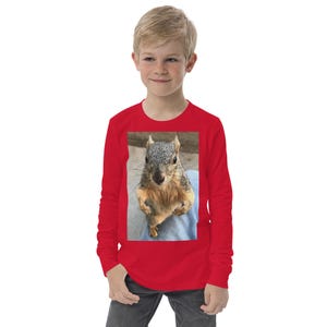Puede incluir: Una camiseta roja de manga larga con una imagen en primer plano de una ardilla. La ardilla tiene pelaje gris y marrón y está de pie. La camiseta está hecha de un material suave y es adecuada para ropa casual.