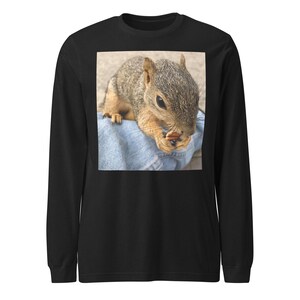 Puede incluir: Camiseta negra de manga larga con una imagen cuadrada de una ardilla comiendo una nuez. La ardilla tiene pelaje marrón y gris y está sentada sobre mezclilla azul. La camiseta tiene cuello redondo.