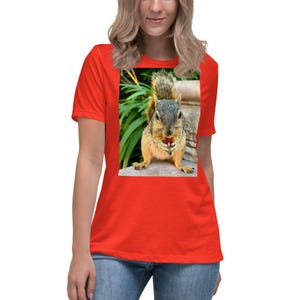 Op de afbeelding: Een rood t-shirt met een afbeelding van een eekhoorn die een noot vasthoudt. De eekhoorn heeft bruine en grijze vacht, tegen een achtergrond van groen en steen. Het shirt is gemaakt van een zacht materiaal.