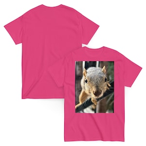 Puede incluir: Una camiseta rosa brillante con una imagen en primer plano de una ardilla. La ardilla tiene pelaje gris y marrón, con una expresión concentrada. La camiseta es de color rosa liso.