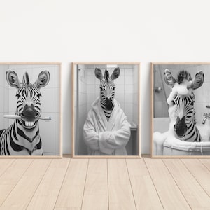 May include: Set of three framed black and white art prints featuring zebras in humorous bathroom scenes. One zebra holds a toothbrush, another wears a bathrobe, and the third is in a bathtub with bubbles. The prints are in wooden frames.