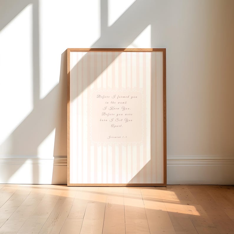 May include: A framed print with a light brown wooden frame. The print features a vertical striped background in light pink and white. The text reads "Before I formed you in the womb, I knew you, Before you were born I set you apart."