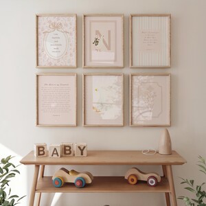 May include: A gallery wall featuring six framed prints with light wood frames. The prints include floral patterns, text, and illustrations in soft pastel colors. A wooden table below displays wooden blocks spelling "BABY" and toy cars.