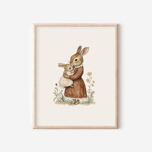 May include: Watercolor illustration of a mother rabbit holding a baby rabbit. The mother rabbit wears a brown dress with a white collar. The background is a soft beige with grass and yellow flowers. The artwork is framed in a light wood frame.