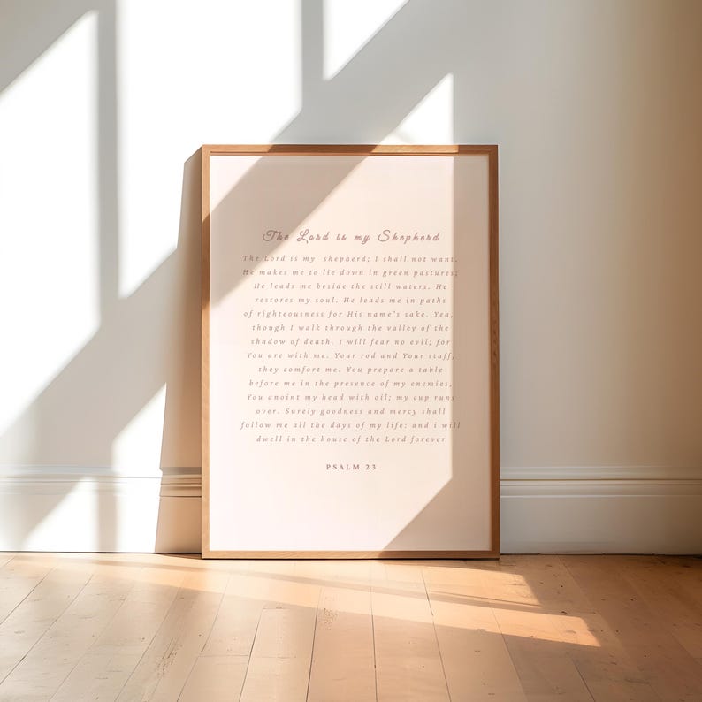 May include: A framed print with the text "The Lord is my Shepherd" and Psalm 23. The text is in a light brown script on a light pink background. The frame is a light brown color.