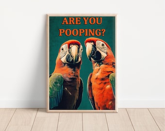 Op de afbeelding: Een ingelijste print met twee kleurrijke ara's met rode, oranje, groene en blauwe veren. De tekst "ARE YOU POOPING?" staat in oranje op een teal achtergrond. Het kunstwerk is gepresenteerd in een houten lijst.