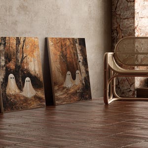 Op de afbeelding: Twee ingelijste canvas prints met een bossc&egrave;ne met spookfiguren. Het kunstwerk gebruikt een warm kleurenpalet van bruin en oranje, met een houten stoel op de achtergrond. De kunst leunt tegen een neutrale muur.