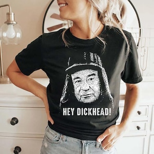 Op de afbeelding: Zwart T-shirt met een zwart-witte afbeelding van een man met een hoed en de witte tekst "HEY DICKHEAD!". Het shirt is een casual stijl.