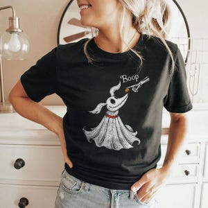 May include: A black short-sleeve t-shirt featuring a white graphic illustration of a ghost dog with a red collar. A skeletal hand reaches out to touch the dog's nose, with the word Boop printed in white script above the dog's head.