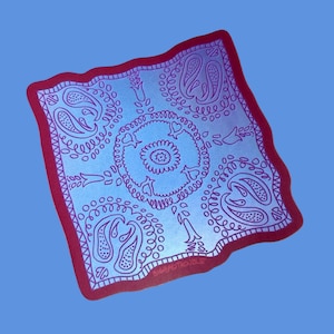 May include: A square, light blue bandana with a red border and intricate purple paisley and floral designs. The center features a circular pattern with a star-like design. The text "BIGBADTROUBLE" is visible in the corner.