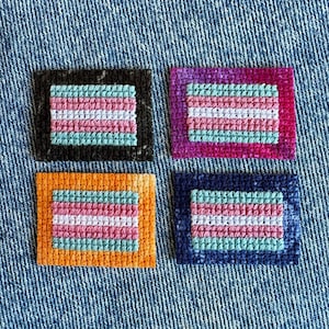 May include: Four rectangular embroidered patches featuring a central striped pattern of light blue, pink, and white. Each patch is framed by a solid border in black, magenta, orange, or dark blue, showcasing a textured cross-stitch fabric design.
