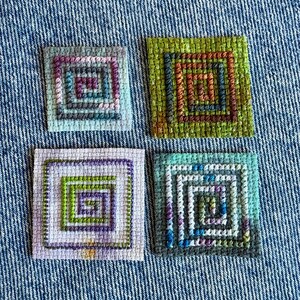 May include: Four square fabric patches featuring hand-stitched embroidery in a spiral pattern. The top left patch is light blue with purple and teal stitching. The top right is lime green with brown and orange. The bottom left is light purple with green and purple. The bottom right is teal with blue and white.