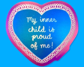 Puede incluir: Pegatina en forma de corazón con un degradado azul y rosa. La pegatina tiene un borde blanco con forma de encaje y el texto "My inner child is proud of me!" en escritura blanca. El fondo es azul brillante.